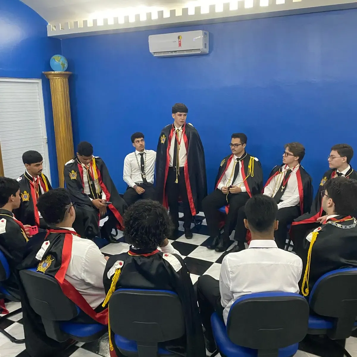 Jovens de capa cerimonial reunidos em círculo durante uma reunião do Capítulo