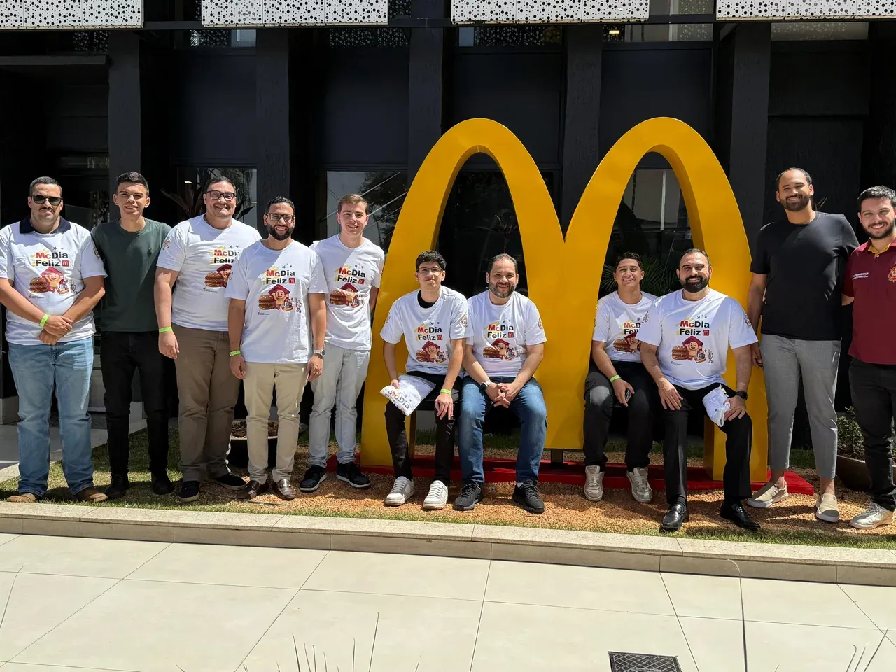 Grupo de DeMolays com camisetas do McDia Feliz posa diante do arco dourado do McDonald's